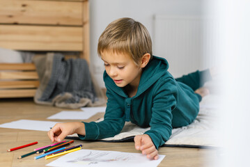 Boy drawing in on the floor a cozy room.