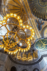 Interior of Hagia Sophia, ornate chandeliers, arches, and domes, historical religious art. Panels with text from Q'ran (verses from Koran holy book in arabic language). Istanbul, Turkey