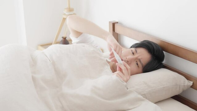寝ながら体温計で熱を測る男性