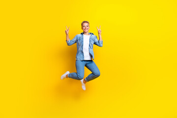 Fototapeta na wymiar Full size photo of pretty young girl jumping show v-sign hello wear trendy jeans outfit isolated on yellow color background