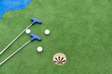 Mini-golf clubs and balls of different colors laid on artificial grass