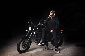 Obraz na płótnie Canvas Portrait of a smoking man sitting on a motorcycle on dark background