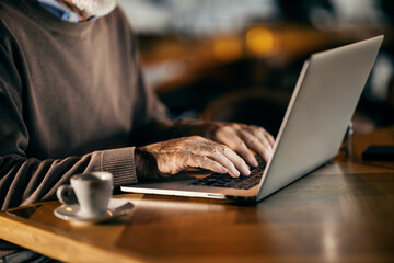 Close up of a senior man's hands typing on a laptop while sitting in cafeteria.