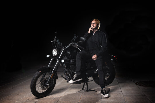 Portrait of a smoking man sitting on a motorcycle on dark background