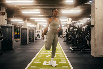 A fit black sportswoman is stretching her legs at the gym.