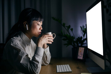 A middle aged japanese businesswoman is working late at home office and drinking her coffee.