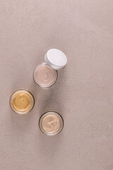 Three beautiful glass cosmetic jars with delicate texture of face and body care cream on a stone beige background. Top Vertical view. A copy space