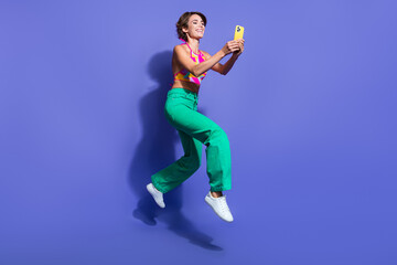 Fototapeta na wymiar Full body length photo of young hipster funny lady jumping with smartphone holding smartphone isolated on violet color background