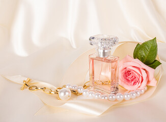 A beautiful composition with an elegant perfume bottle, pink roses, a gold necklace and a satin ribbon. Delicate satin beige background.