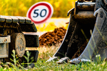Arm of a mini digger and bucket with a speed limit sign at 50, road sign