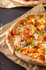 Fresh beautiful appetizing pizza with smoked sausage and green peppers, onions and sauce on craft paper on a black background close up