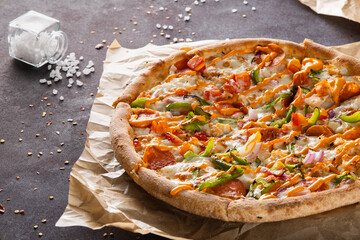 Fresh beautiful appetizing pizza with smoked sausage and green peppers, onions and sauce on craft paper on a black background close up