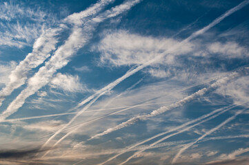 Gewirr von sich teilweise auflösenden Kondensstreifen am blauen Himmel mit leichter Bewölkung und Cirruswolken