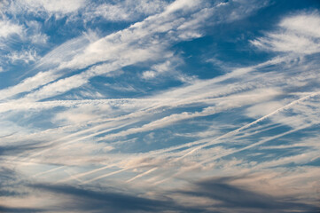 Viele, sich teilweise kreuzende Kondensstreifen am blauen Himmel mit aufgelockerter Bewölkung und Cirruswolken