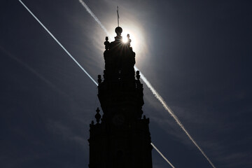 Clerigos Church tower silhouette in Porto against direct sun and plane cloud tracks on the sky....