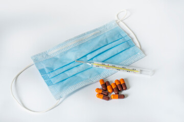 protective medical mask, thermometer and pill capsules on a white background. View from above.