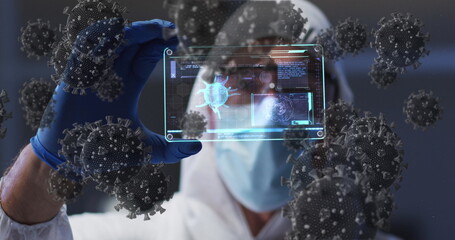Image of covid 19 cells over scientist in ppe suit holding screen with medical data processing