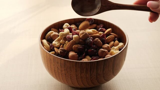 Bowl filled with mix assorted nuts and dried fruits sits on table, as spoon scoops up crunchy delights Dive into rich flavors and textures of nuts with every spoonful Enjoy wholesome goodness of nuts