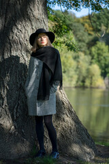 A young girl in a black hat standing against a background of wood texture near a lake