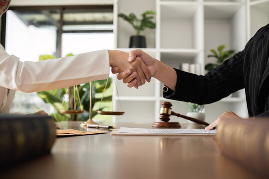 A lawyer and a businesswoman shake hands and reach an agreement on a cooperation contract document. In the lawyer's office and there is a hammer lying on the table.