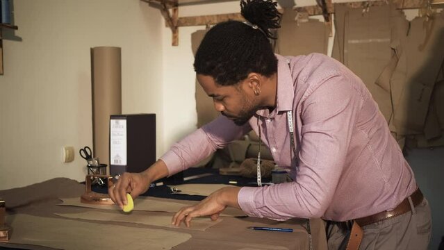 Male fashion tailor working on the measurements for the suit design in his workshop.