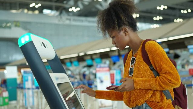 African woman holding passport using self Check-in kiosk machine getting airline ticket boarding pass at airport terminal. People travel on holiday vacation and global airplane transportation concept.