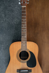 Acoustic guitar on a textured black and wooden background, top view.