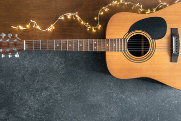 Acoustic guitar and garland on a textured black and wooden background, top view.