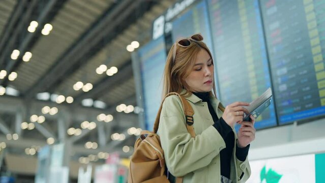 Asian woman passenger looking flight schedule on timetable and go to check-in and boarding gate in airport terminal. Attractive girl traveler travel by airplane transportation on holiday vacation.