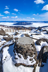 爽快な青空と雪に覆われた岩場と眼下の氷に覆われた湖。爽やかな印象の冬景色。北海道の美幌峠展望所から見下ろす屈斜路湖。