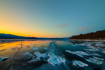 夕暮れの空の色を反射する氷に覆われた湖。結氷した湖面の雪の風に流された模様。北海道の屈斜路湖。 - obrazy, fototapety, plakaty