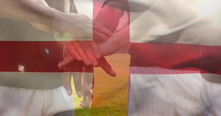 Image of flag of england and confetti over diverse male soccer players teaming up at stadium