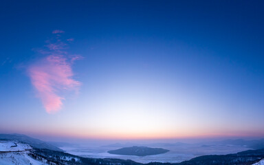 Obraz premium 広い夜明けの空の下の朝もやに霞んだ峰から見下ろす結氷した湖。北海道の美幌峠から見る屈斜路湖。