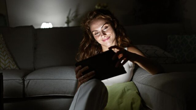 A serene woman enjoys reading on her tablet in a cozy living room at night.