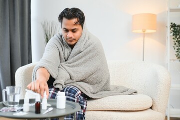 Sick Indian man in plaid sit alone shivering from cold. Unhealthy Arabian guy sit on chair feeling...
