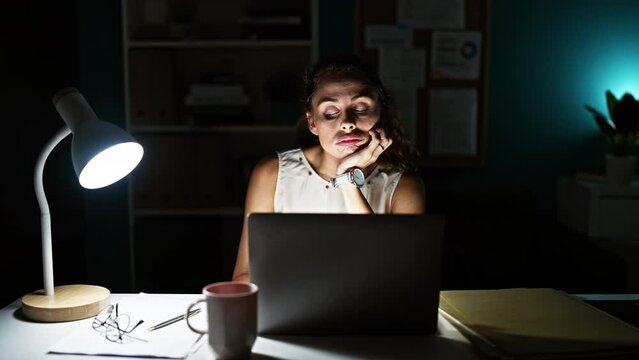 A young woman in an office balances a pen on her upper lip, making a funny face at night.
