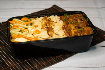 Chicken Bhuna with pulao biryani rice with cucumber, dip sauce and lemon slice served in dish isolated on wooden table side view closeup of bangladeshi and indian spicy lunch food