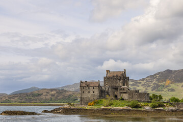 Clouds drift above Eilean Donan Castle, a monument of Scottish heritage poised on the water's edge, framed by the rolling hills of the Highlands