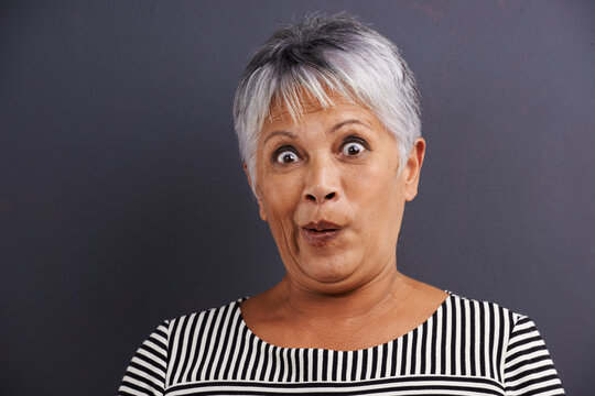 Surprise, portrait and senior woman in studio with crazy, silly or crazy facial expression for comedy. Shock, comic and elderly female person with wow, omg or wtf face isolated by gray background.