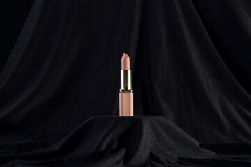 nude matte lipstick on podium on black background in a pink and gold tube top view. Professional...