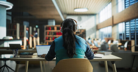 Female Student Wearing Headphones while Working on University Homework in a Public Library. Woman...
