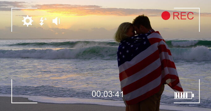 Naklejki Young couple wrapped in American flag on beach, captured on camera in 4k.