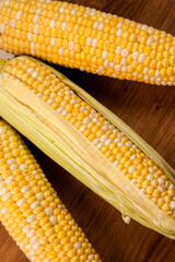 Clous up view of cutting board with three cobs sweet corn on white wooden background..