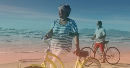 Spots of light against african american senior couple with bicycles walking together at the beach