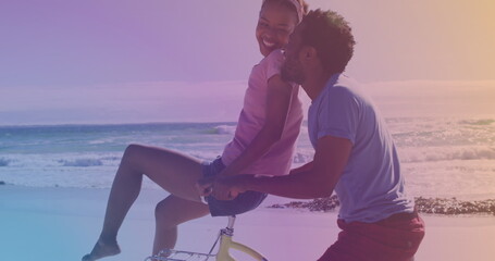 Spots of light against african american young couple riding in a bicycle together at the beach