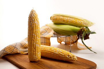 Cutting board with two cobs sweet corn on white wooden background..