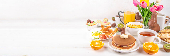 Easter holiday sweet breakfast, brunch. Easter decorated belgian waffles, pancakes, breakfast cereals and milk, fried eggs with toasts and bacon, Easter chocolate eggs and bunny, with spring flowers - obrazy, fototapety, plakaty