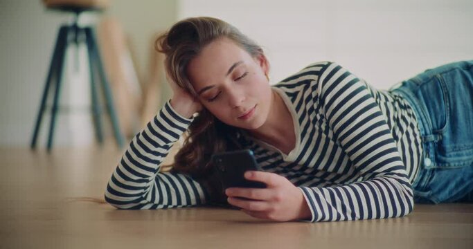 Beautiful woman texting through mobile phone while lying on floor