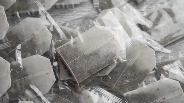 New unused tea bags with dried herb leaves with transparent polythene packs falling in slow motion close up
