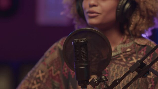 Closeup of female podcast host fixing pop screen while talking during record in neon lit studio at night